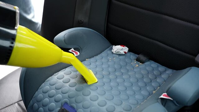 Car wash worker cleaning child car seat with vacuum cleaner, cleaning seat from crumbs, candy wrappers and debris left after child ride in car. Concept of cleanliness in car interior