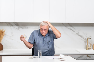 Close up of unhappy elderly man sitting at the table, stressed and confused by calculate expense from invoice or bills, have no money to pay mortgage or loan. High prices and spending money concept