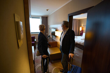 Adult businessman and businesswoman standing and looking inside hotel room