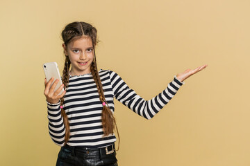 Young preteen child girl kid with mobile smartphone showing pointing empty place, advertising area for commercial text, copy-space for apps promotion. Teenager children isolated on beige background