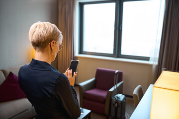 Back view of businesswoman using mobile phone in hotel room at daytime