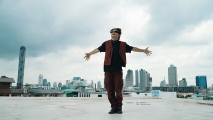 Motion shot of B-boy dance performance by professional street dancer at rooftop with sky scrapper,...