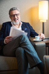 Laughing adult caucasian businessman with papers drinking tea or coffee from cup