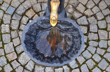 An old black metal (vintage) drinking fountain shellfish shape (shaped) with golden tap, top view on a pavement background