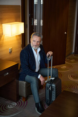 Fototapeta na wymiar Concentrated businessman with suitcase sitting on leather chair and looking away