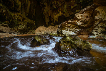 Fototapeta premium The beautiful views of the stalactite and stalagmite-filled cave in Lam Khlong Ngu National Park, Thailand. At the cave's exit is a small waterfall also.