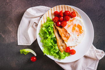 Close up of tacos with fried egg, bacon, tomato and lettuce on a plate on the table top view