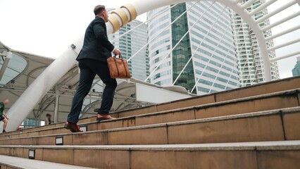 Smart caucasian businessman walking up stairs surrounded by urban view. Side view of ambitious...