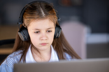 Portrait of a cute girl wearing headphones sitting at a laptop.