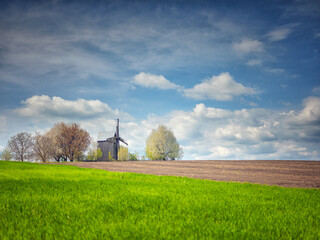 spring day in farmland with view to fields, sky and old wooden mill