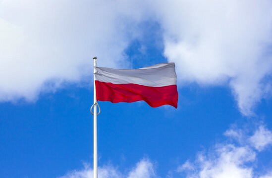 National flag of Poland on a flagpole over blue sky with clouds an copy space for text or design.