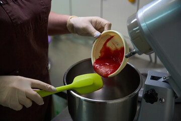 Confectioner pouring fresh berries puree into mixer bowl
