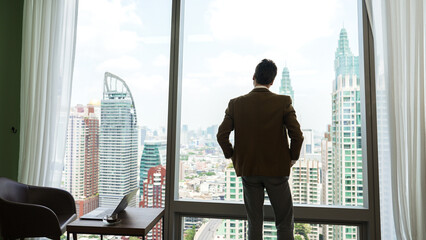 Back view ambitious businessman standing in ornamented office gazing out window to cityscape...