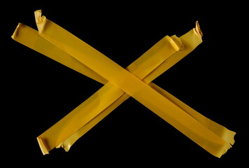 Yellow adhesive tape strips in shape cross, isolated on black background, top view