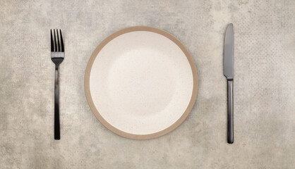 Empty beige gray plate, fork; knife on marble rustic concrete background. Top view, flat lay.