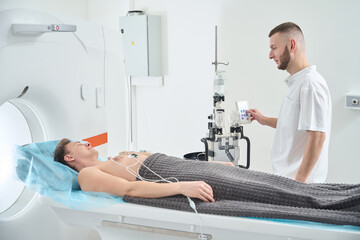 Obraz premium Doctor preparing man for contrast-enhanced ECG-gated coronary CT angiography