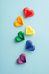 Vivid vertical multi-colored paper hearts arranged in a floating pattern on a gentle blue backdrop,...
