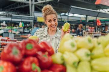Portrait of a happy woman at food market showing fresh pepper at camera