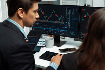 Two business traders discussing on dynamic stock market in currency rate investment trading on two pc screens with compare real time graph on risk or profit point of data at modern office. Postulate.