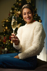 Young pleased woman with champagne in glass looking at camera during Christmas