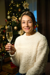 Happy beautiful woman with champagne in glass looking at camera during Christmas