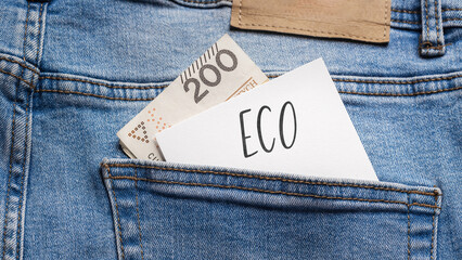 White card with a handwritten inscription "Eco", put into the pocket of blue pants jeasnow, next to Polish banknotes PLN (selective focus)