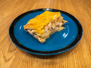 A piece of Potato casserole with mushrooms and chicken covered by cheese crust on the dark blue...