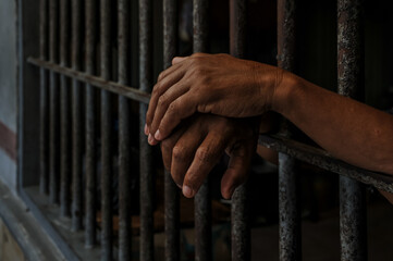 hands of a prisoner behind prison bars