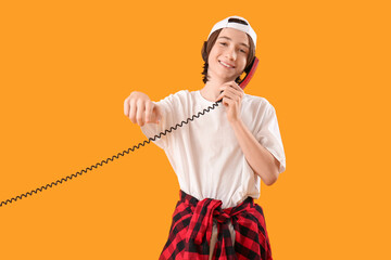 Cool teenage boy with phone receiver pointing at viewer on yellow background