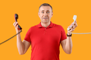 Surprised mature man with phone receivers on yellow background