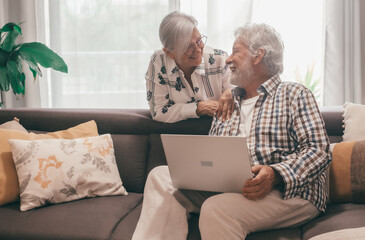 Relaxed senior white haired couple sitting on home sofa using computer have fun together enjoying...