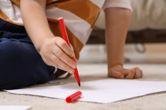 Cute little boy drawing with felt-tip pens on floor at home, closeup