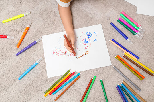 Cute little boy drawing with felt-tip pens on floor at home, top view