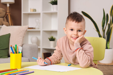 Cute little boy drawing with felt-tip pens at table in room
