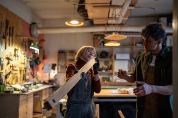 Interested couple carpenters in joinery workshop examines part of handmade product. Craftswoman with work partner checks evenness of wooden block furniture assembled. Small woodwork business. Teamwork