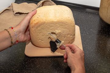 loaf of freshly baked homemade bread from a bread machine. The housewife takes out a knife from the loaf to knead the dough.