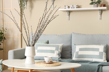 Vase with willow branches and cup of tea on table in living room