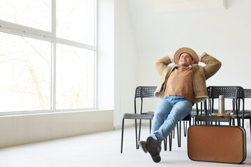 Male tourist in winter clothes resting in chair at airport