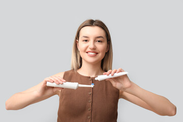 Young woman pouring tooth paste onto electric brush on light background - obrazy, fototapety, plakaty