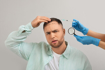 Young man with hair loss problem and marks receiving injection on grey background