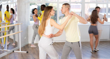 Cheerful fit young woman practicing passionate samba with interested attentive man in dance class for adults. Amateur dancing concept.. - obrazy, fototapety, plakaty