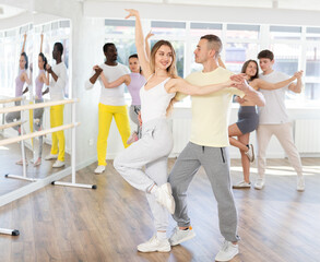 Positive young pair engaged in salsa dance together with other attendees of dancing courses