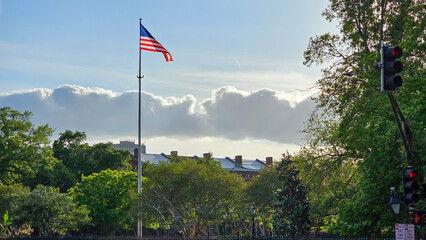 An American flag flying at sunset surrounded by lush green trees, blue sky and clouds in the French Quarter in New Orleans Louisiana USA