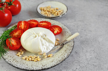 burrata with tomatoes. Caprese salad with tomatoes, burrata cheese and pine nuts. Cutaway soft cheese in a burrata bag. Close-up