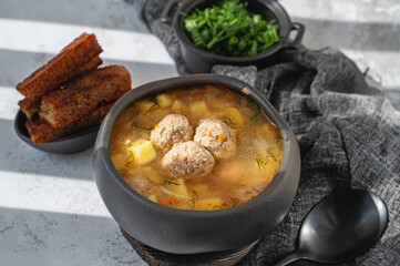 Meatball in a spoon. soup with meatballs in a black bowl and croutons in hard light. A European dish typical of Spain, Sweden, Turkey, and Russia. Meatballs, kyufta, faggots - meat balls in soup