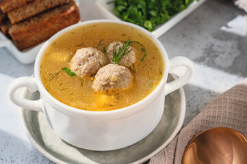 White broth bowl with handles with delicious meatball soup with croutons and herbs on a wooden...
