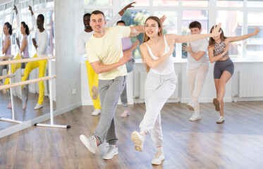 Smiling enthusiastic young adult woman and man in activewear rehearsing upbeat jive dance moves as...