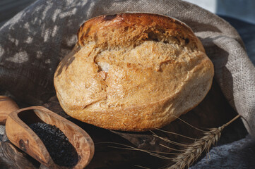 Round white bread. Close-up of white bread with homemade black salt in a wooden scoop on a light marble background. Close-up