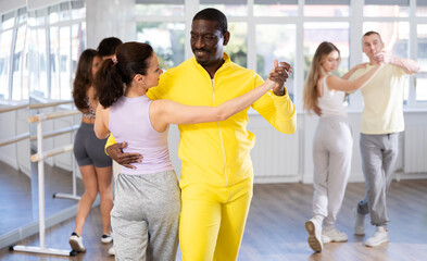 Slim middle-aged man and woman practicing waltz dance in training hall during group dancing classes