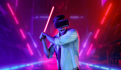 Gamer holding laser sword and playing action game while wearing VR glasses. Caucasian man using...